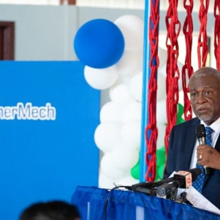 A man in a suit speaks at a podium with a microphone. Behind him are colorful balloons and a "3t EnerMech" sign.