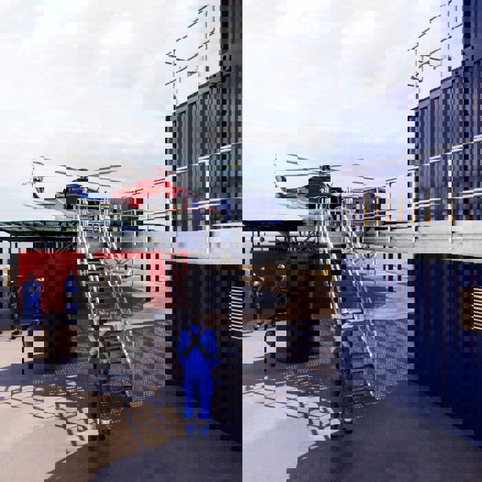 Helicopter on a platform with workers in blue uniforms nearby, situated beside metal containers.