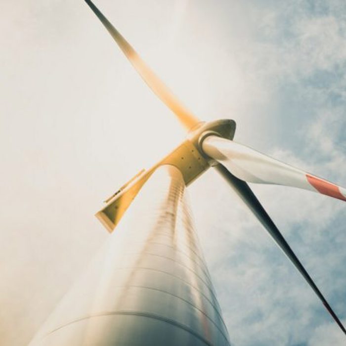 Low-angle view of a wind turbine against a cloudy sky with sunlight illuminating the blade tips.
