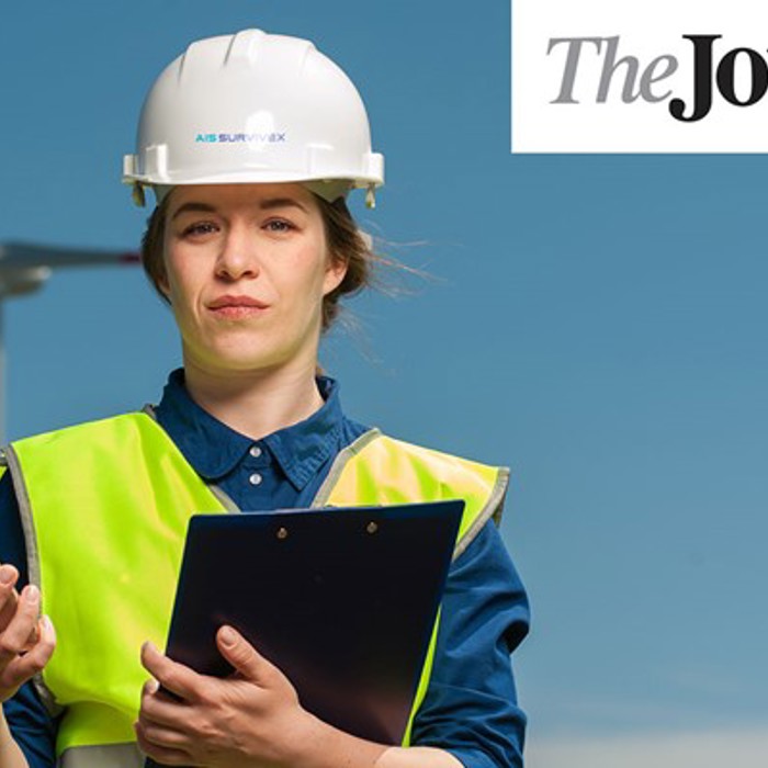 A person in a hard hat and high-visibility vest stands with a clipboard and phone, with a wind turbine in the background. "The Journal" logo is in the upper right corner.