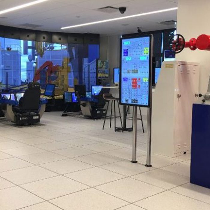 A modern control room featuring multiple workstations with computer monitors, a large digital display wall, and various control panels and industrial equipment.