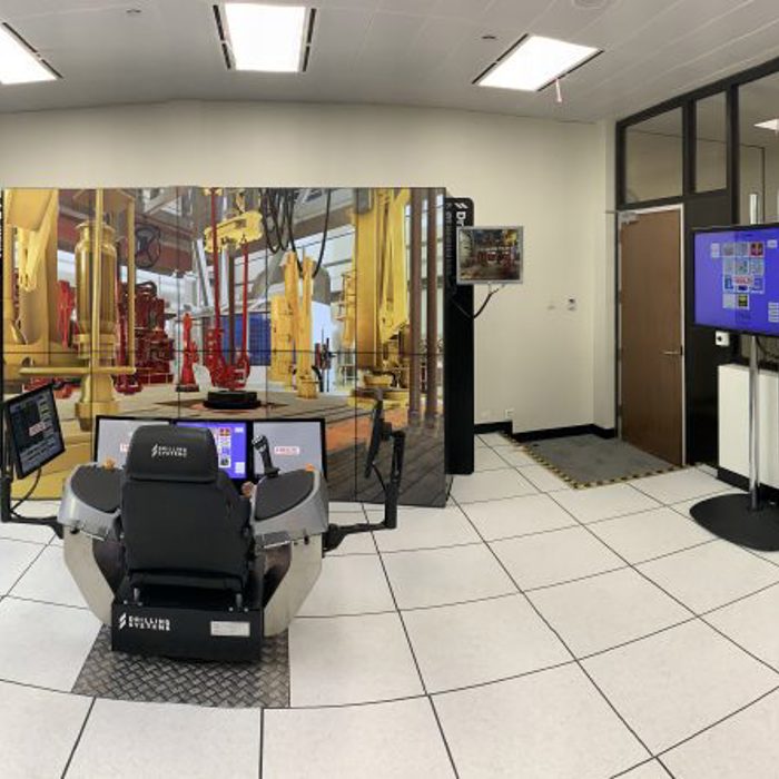 A room with a simulator setup, featuring a central control chair, multiple screens displaying various interfaces, and several other technical equipment and monitors around the room.