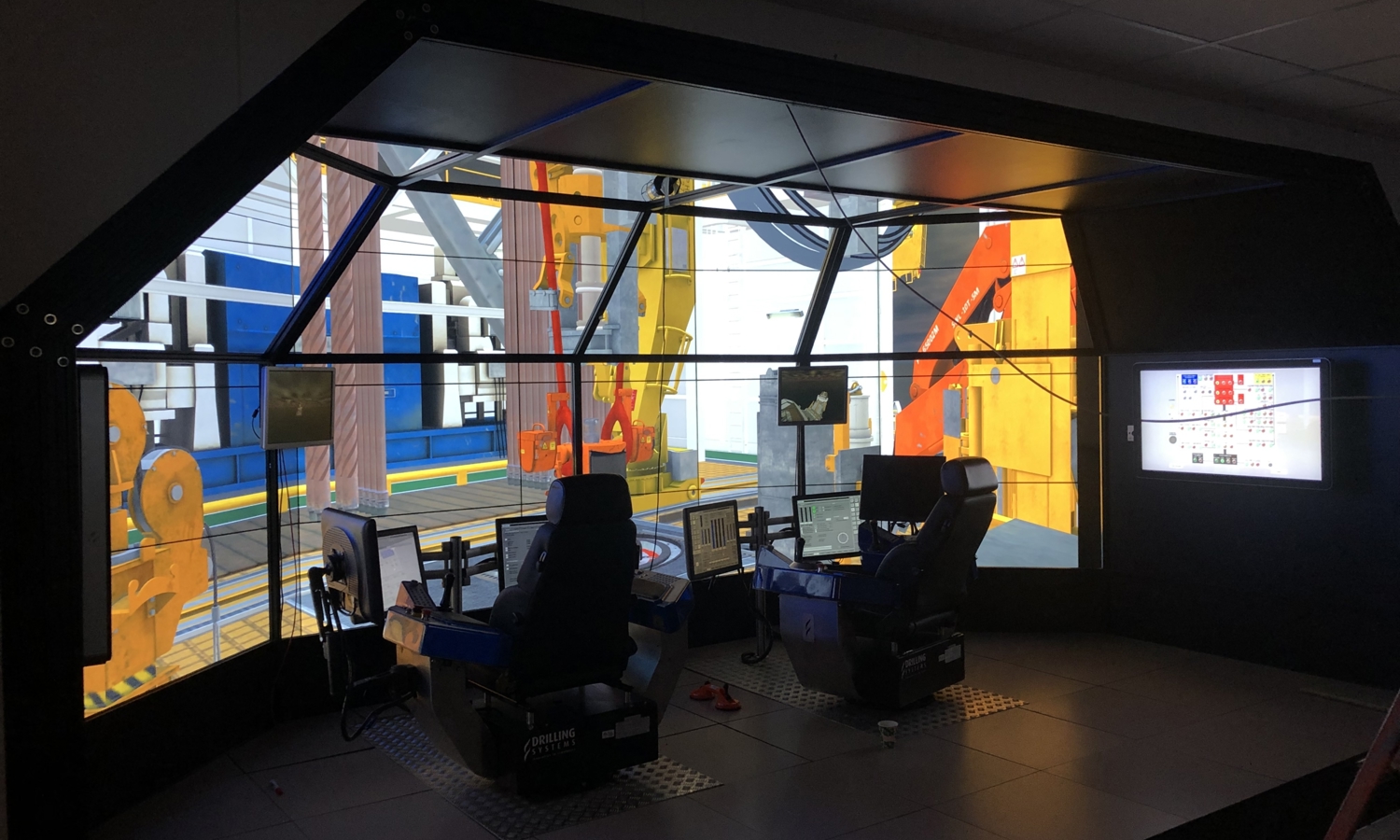 A modern simulation room with two control stations surrounded by large screen displays depicting an industrial environment.