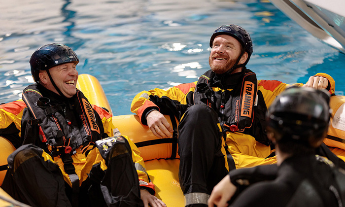 People wearing protective suits and helmets sit in an inflatable raft in a pool, honing their skills during a training exercise.