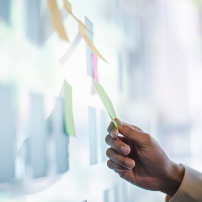 Uma mão arruma metodicamente notas autocolantes coloridas numa superfície de vidro, como se estivesse a preparar o terreno para uma sessão de treino criativo.