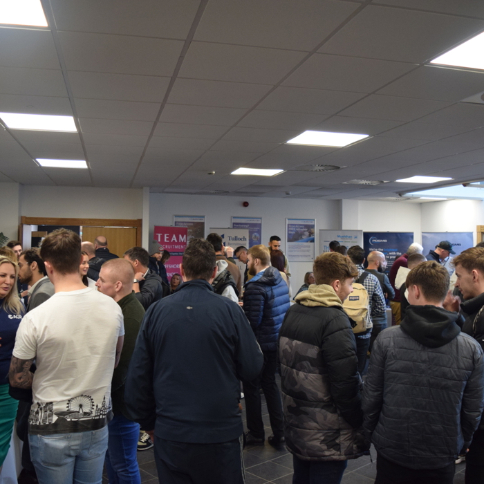 A group of people mingling in a conference room, engaging in conversations near informational booths and banners promoting upcoming training sessions.