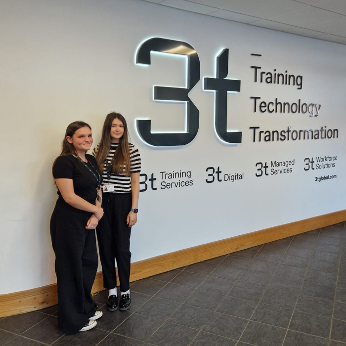Two people stand in front of a wall adorned with the bold 3t logo and the phrase: "Training, Technology, Transformation," highlighting our specialized training services and related offerings.
