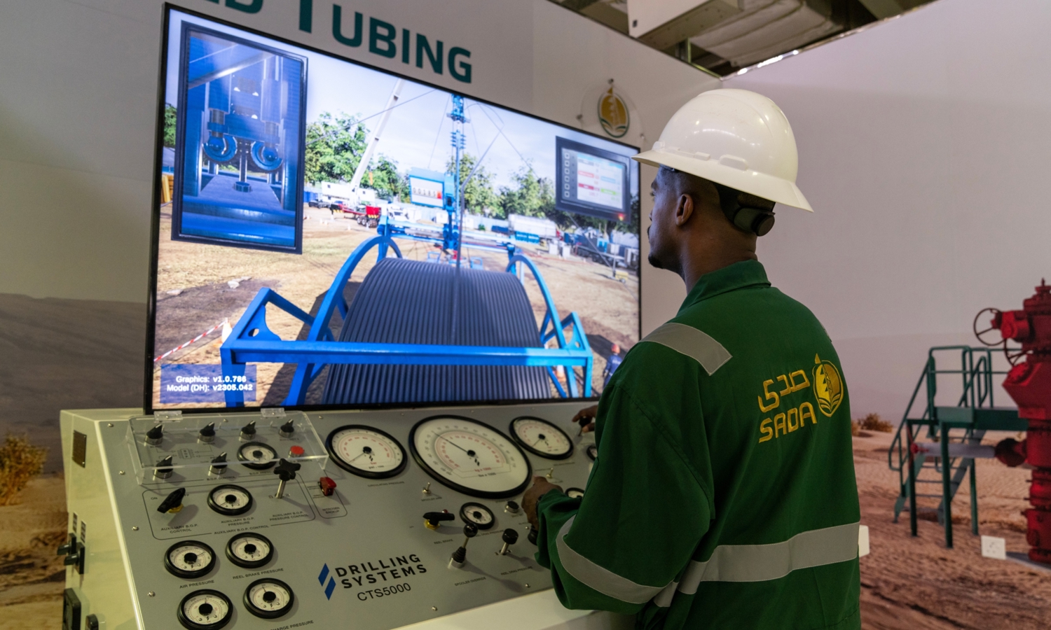 A person in a hard hat operates a sophisticated drilling simulation console with gauges, engaged in an advanced training session, as a large screen vividly displays an oilfield scene.