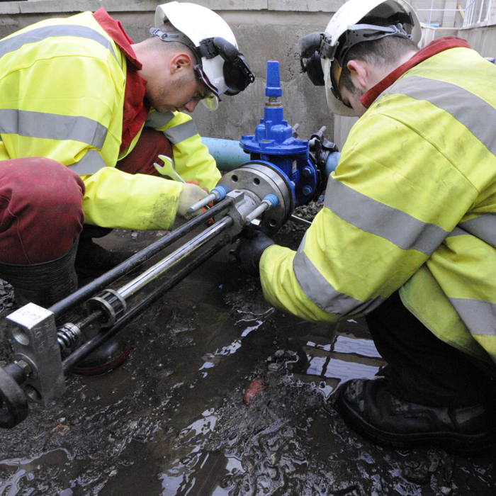 Two workers in safety gear, utilizing their training, repair a pipe outdoors, surrounded by wet ground.